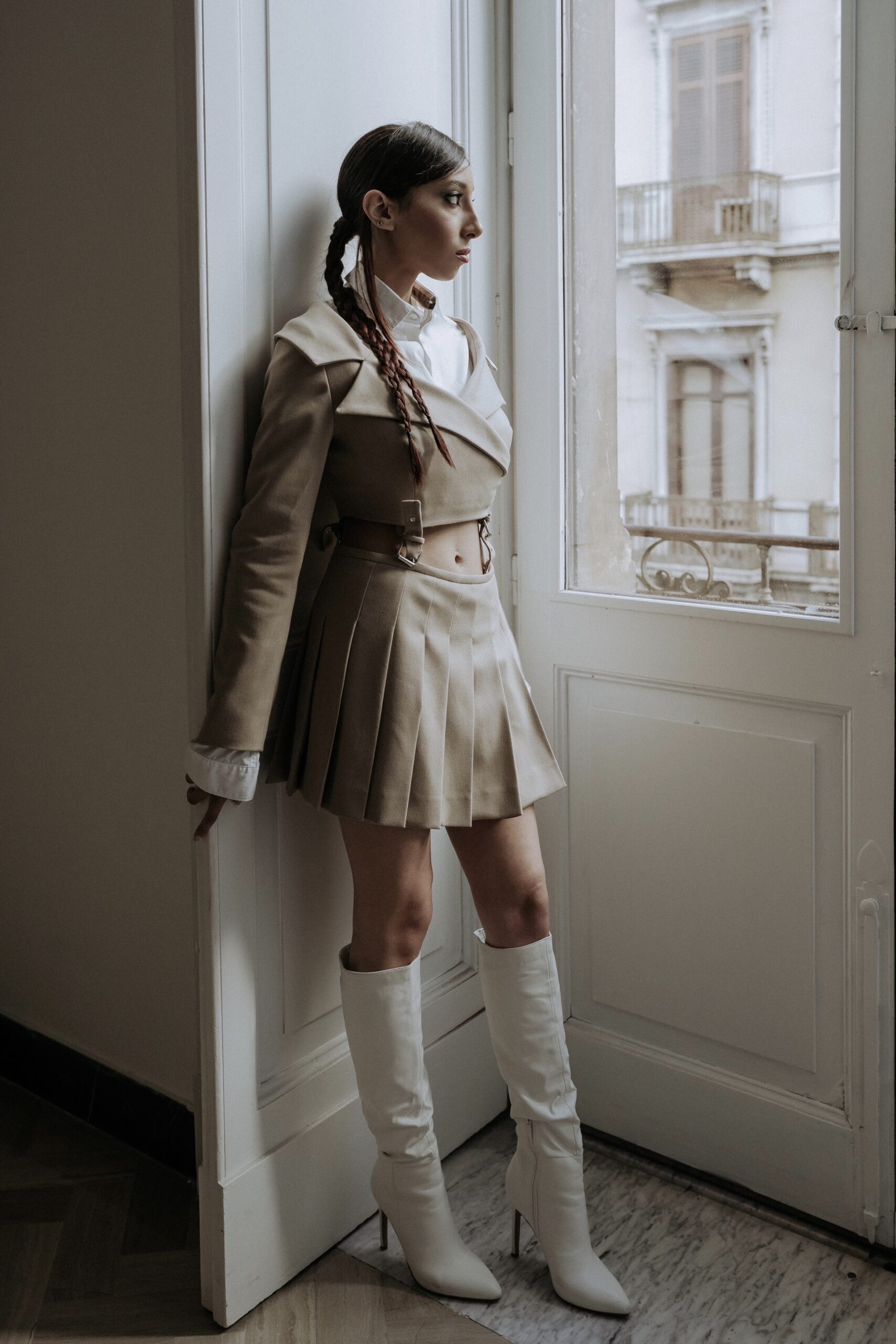 Modella indossa un completo a fibie LegameBrand, composto da blazer e minigonna, mentre guarda attraverso una finestra con determinazione e stile.